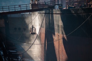 Dockworker powerwashing side of ship