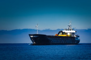 Black cargo ship with industrial excavator onboard sailing in daytime