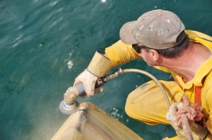 Maritime worker using wire brush to clean hull of ship