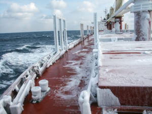 Cargo vessel in motion in icy waters with ice and snow on deck of boat